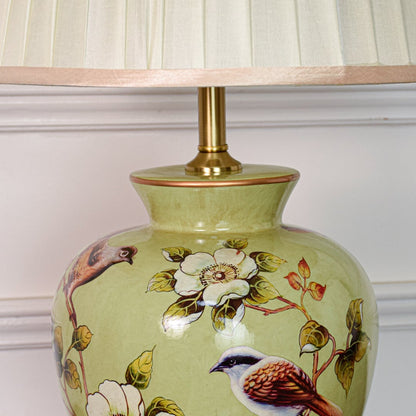 Closeup of green ceramic table lamp highlighting hand painted birds floral motifs smooth glaze finish and brass base.