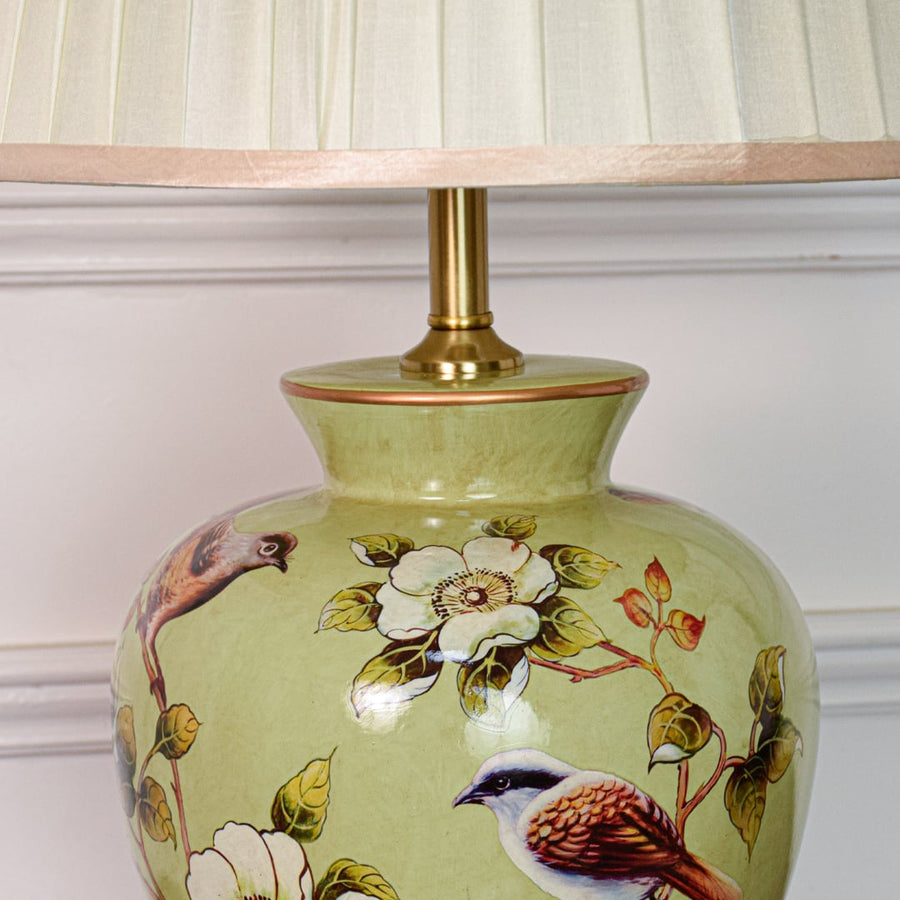 Closeup of green ceramic table lamp highlighting hand painted birds floral motifs smooth glaze finish and brass base.