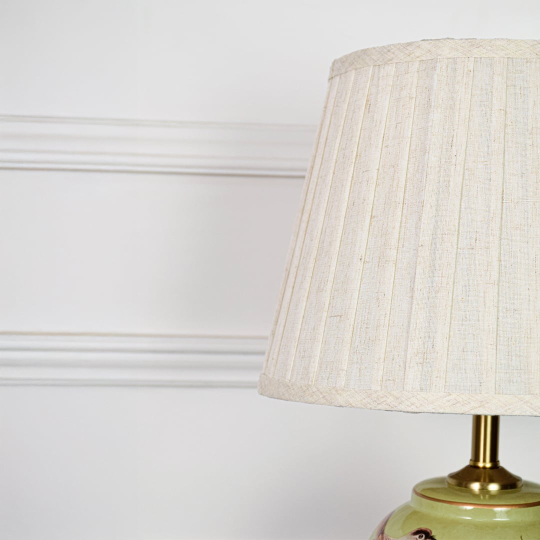 Closeup of green ceramic table lamp showing detailed hand painted birds floral pattern smooth glaze and brass base.
