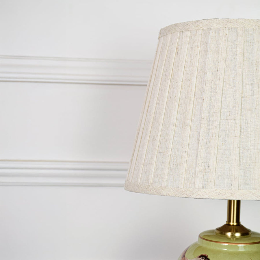 Closeup of green ceramic table lamp showing detailed hand painted birds floral pattern smooth glaze and brass base.