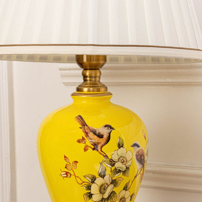 Table lamp closeup showing yellow ceramic base with floral artwork and gold detailing for refined interior accents.