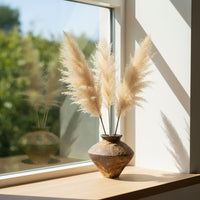 Handcrafted ceramic decorative vase styled on a wooden window ledge with dried pampas grass creating a warm minimalist home Decor setting.