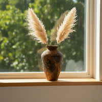 Decorative ceramic vase styled on a window sill with dried pampas grass adding a warm organic accent to a sunlit interior setting with soft natural light.