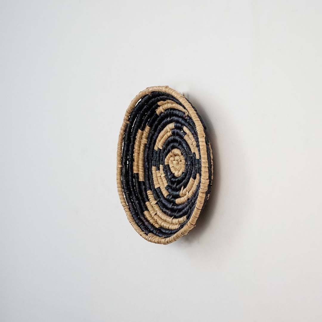 Handwoven seagrass round wall basket decor in natural beige and black with raised spiral woven profile on white background.
