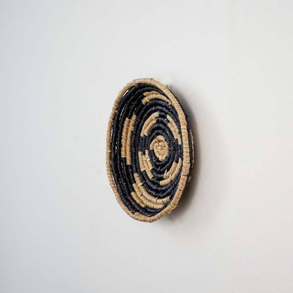 Handwoven seagrass round wall basket decor in natural beige and black with raised spiral woven profile on white background.