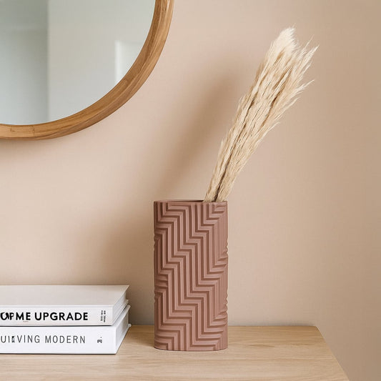 A modern textured beige vase displayed on a wooden surface against a patterned wall adding a warm stylish accent to contemporary home decor.