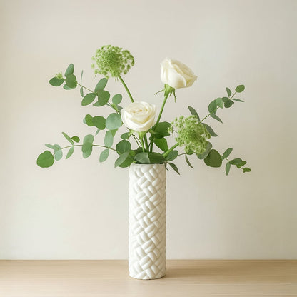 White ceramic decorative vase with braided texture placed on wooden table holding white roses and green eucalyptus stems for modern home decor.