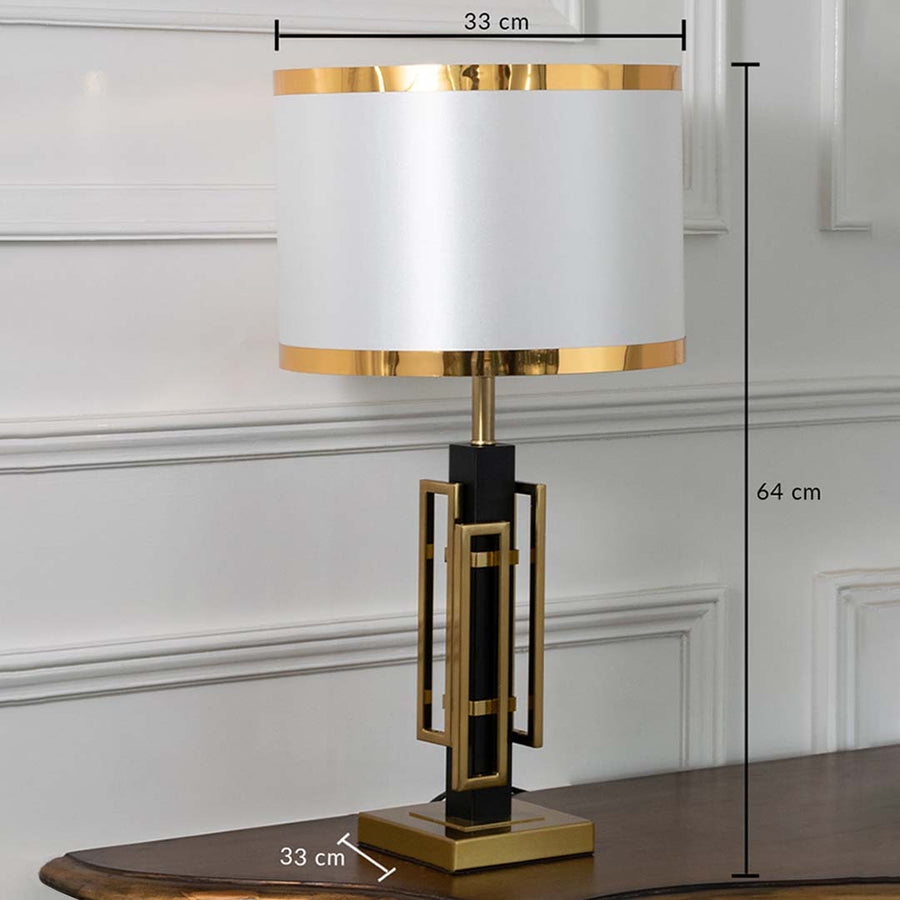 Black and gold geometric table lamp with white drum shade shown with clear dimensions of 33 cm width 64 cm height and 33 cm depth ideal for bedside or console spaces.