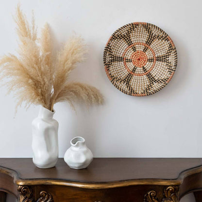 Bohemian style woven seagrass wall basket hanging above a wooden console table decorated with vases and pampas grass.