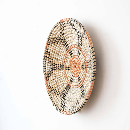 Side angle view of a floral pattern woven seagrass wall hanging basket plate showing depth structure on a white wall.
