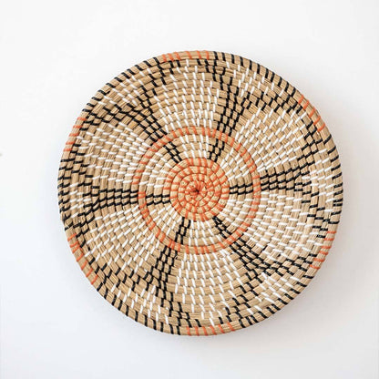 Beautiful orange and black floral patterned woven seagrass wall basket plate decoration isolated on a white backdrop.
