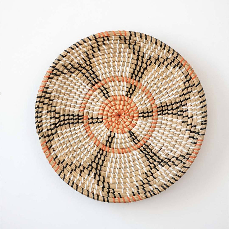 Beautiful orange and black floral patterned woven seagrass wall basket plate decoration isolated on a white backdrop.