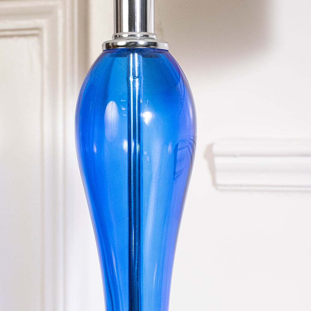 Closeup of blue glass lamp showing glossy base chrome detailing and fabric shade designed for modern home decor.