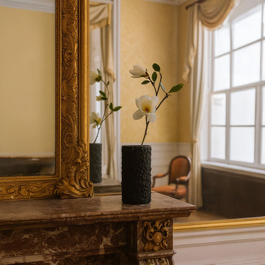 Black cylindrical textured ceramic vase styled with a single white flower displayed on a marble console in an elegant interior.