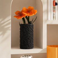 Contemporary black woven ceramic vase holding bright orange flowers displayed inside a modern geometric wall shelf alcove.