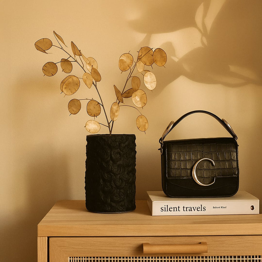 Black cylindrical textured ceramic vase styled with a single white flower displayed on a marble console in an elegant interior.