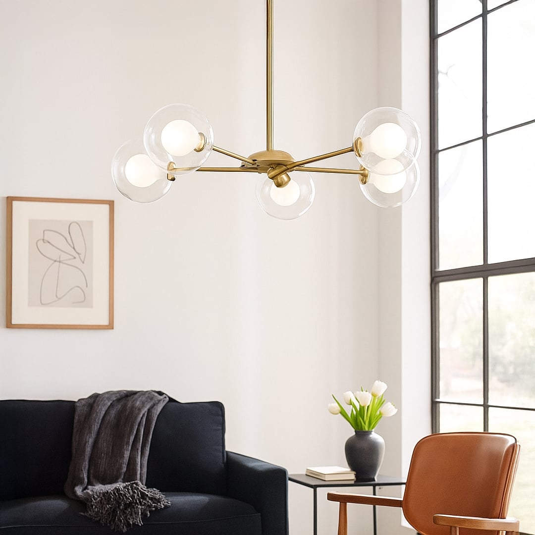 Gold metal chandelier with clear glass globe shades creating warm ambient lighting in modern living room interiors.