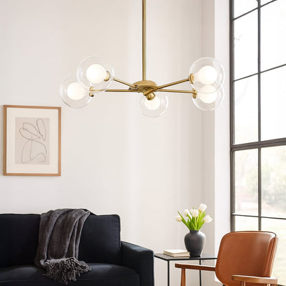 Gold metal chandelier with clear glass globe shades creating warm ambient lighting in modern living room interiors.