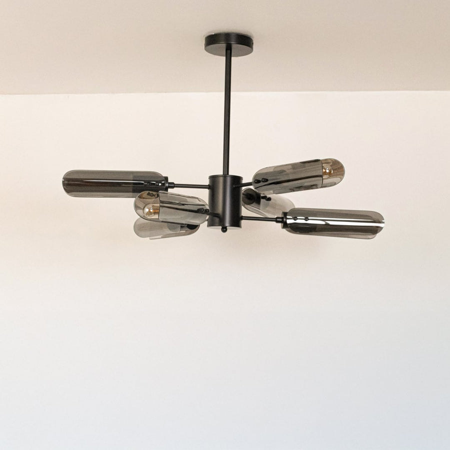 Black metal chandelier with smoky grey glass tubes displayed off on white background showcasing sleek modern lighting design.