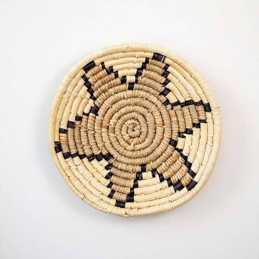 Handwoven seagrass round wall basket decor in natural beige and black with spiral star woven pattern on white background.