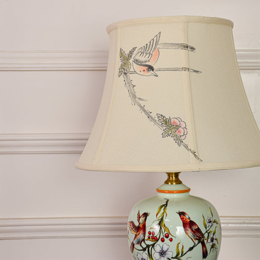 Closeup of mint green ceramic table lamp highlighting detailed bird floral artwork smooth glaze and gold metal finish.