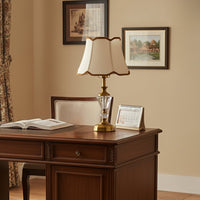 Classic table lamp with gold metal and crystal base placed on a wooden study desk creating warm ambient lighting in a traditional home interior.