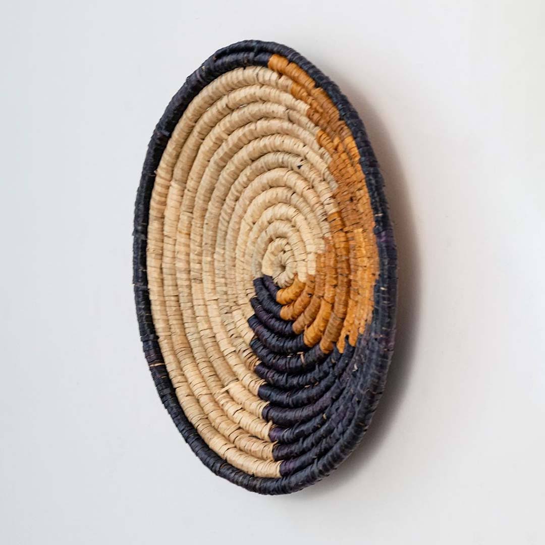 Handwoven seagrass round wall basket decor in natural beige black and mustard with raised woven profile on white background.