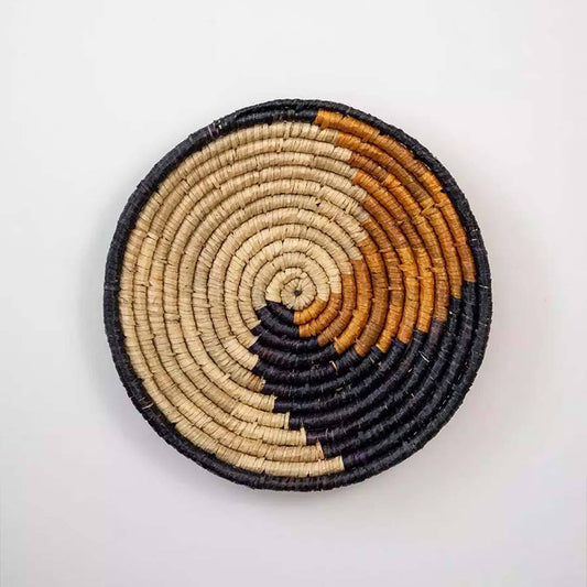 Handwoven seagrass round wall basket decor in natural beige black and mustard with spiral woven pattern on white background.