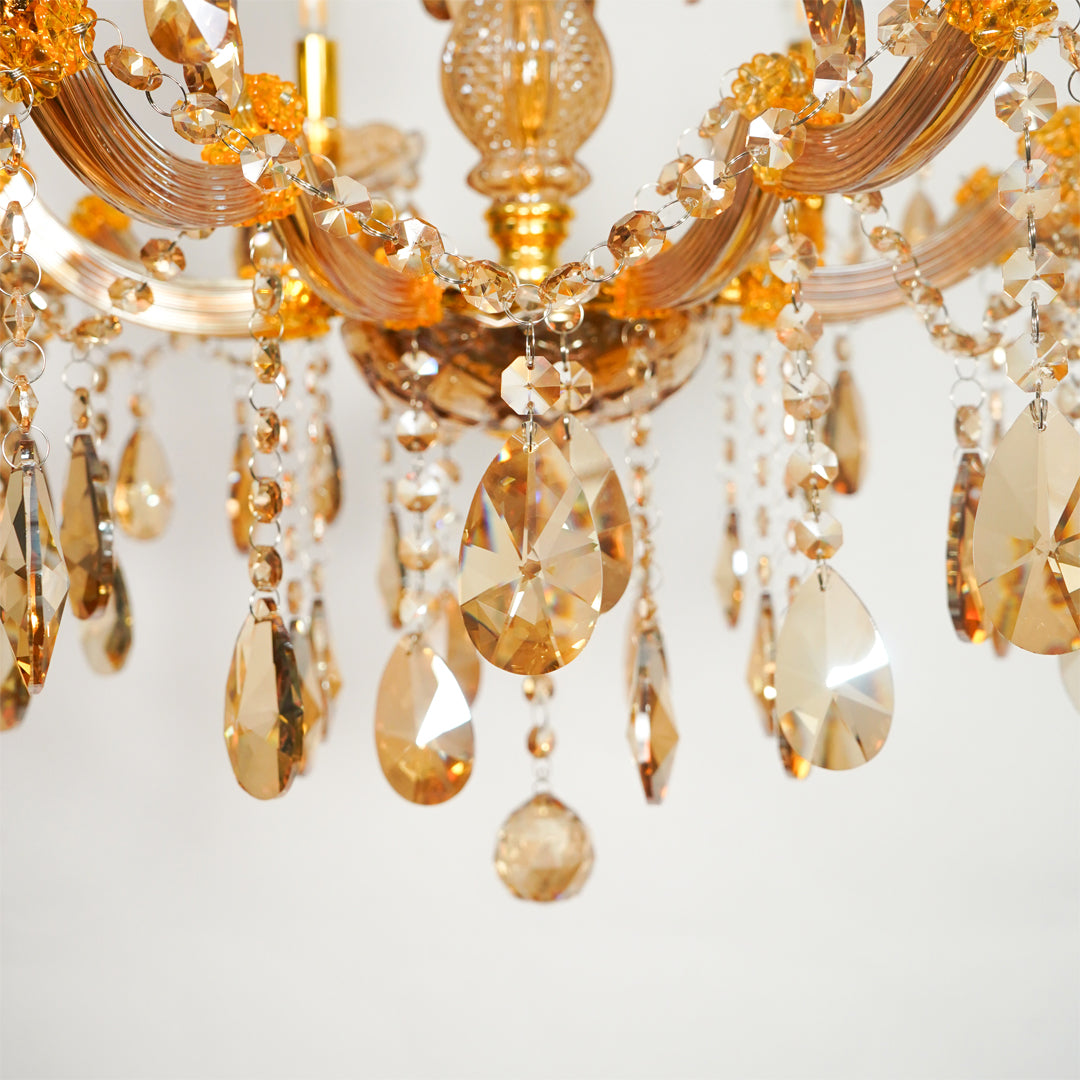 Close-up of a chandelier with curved gold-toned arms and cascading faceted crystal drops in amber, champagne, and clear tones against a soft light background.