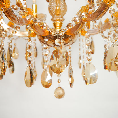 Close-up of a chandelier with curved gold-toned arms and cascading faceted crystal drops in amber, champagne, and clear tones against a soft light background.