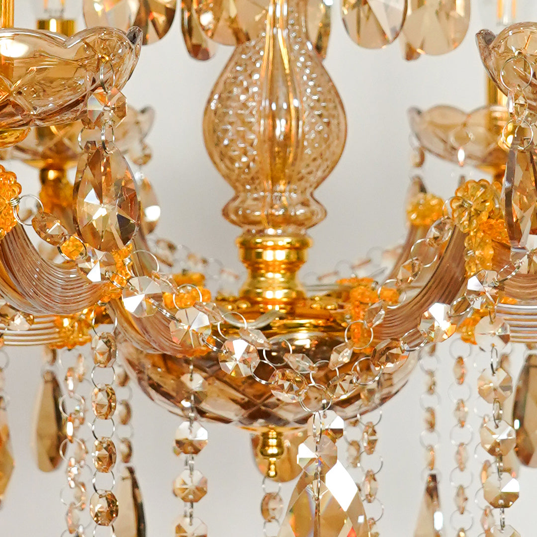 Close-up of an amber glass chandelier with faceted crystal drops and warm gold-toned metal details against a light neutral background.