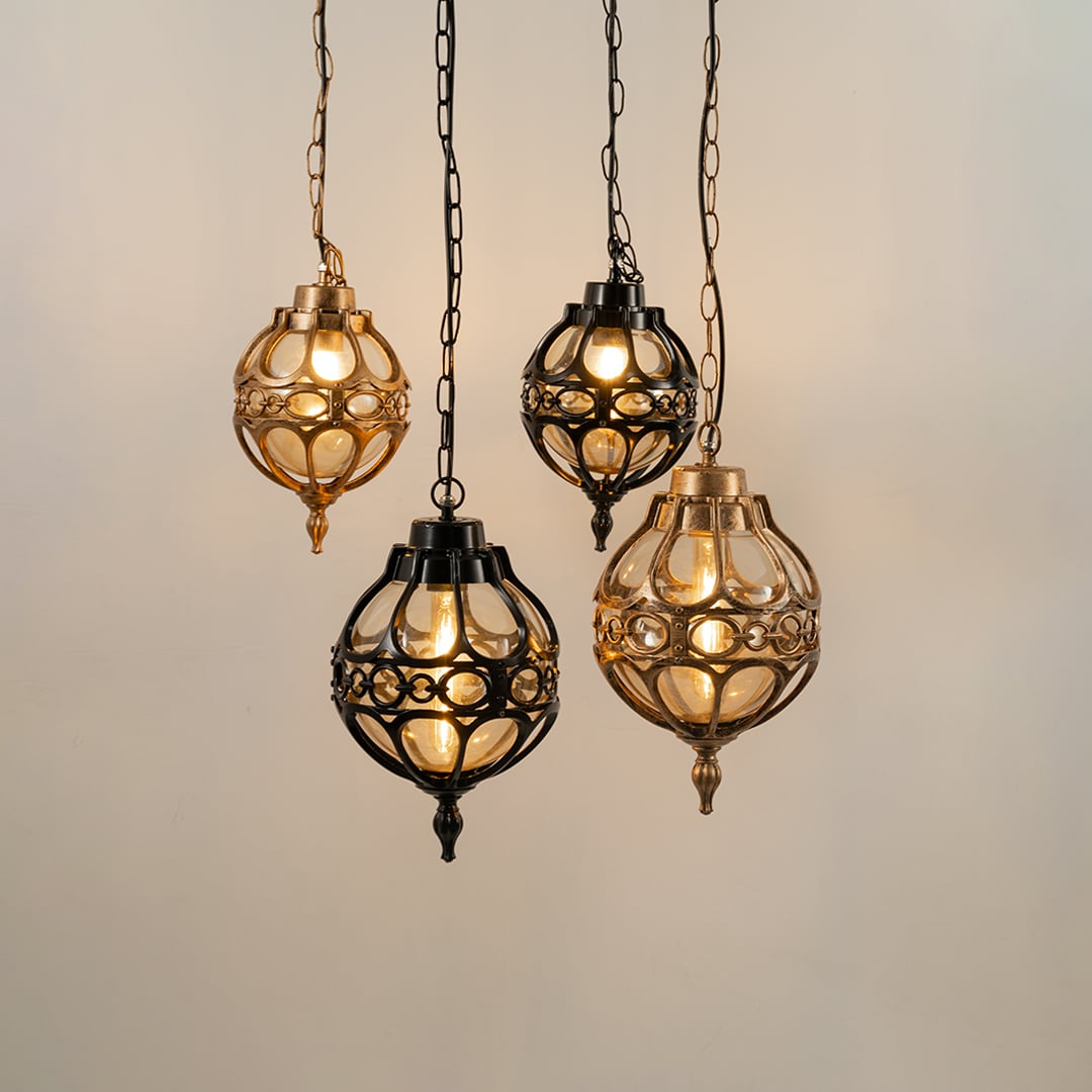 Group of four vintage style round cage pendant lights in black and gold finishes hanging together with warm lights on.