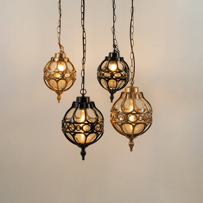 Group of four vintage style round cage pendant lights in black and gold finishes hanging together with warm lights on.