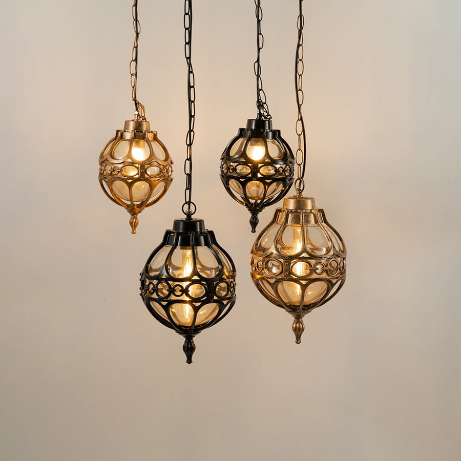Group of four vintage style round cage pendant lights in black and gold finishes hanging together with warm lights on.