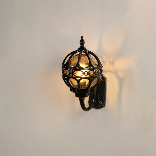 Vintage black outdoor wall sconce on white background featuring an ornate metal globe cage casting a dramatic radial glow.