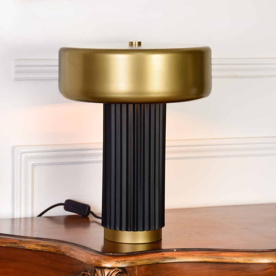 Table lamp displayed on clean white background showing brushed gold shade and vertical ribbed black base highlighting modern design and premium finish.