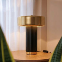 Gold metal table lamp with ribbed black base casting warm ambient light on bedside table in elegant interior.