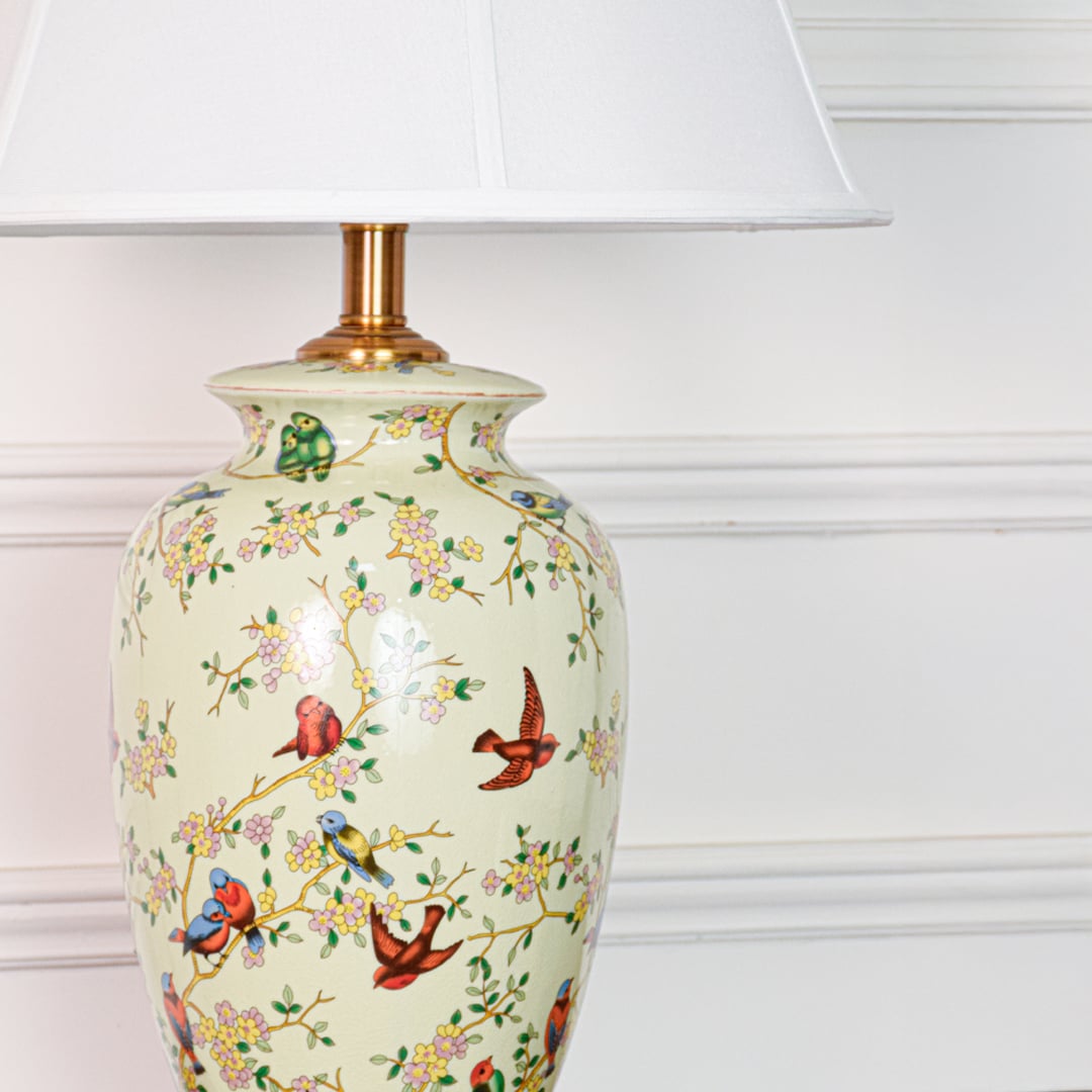 Closeup of green ceramic table lamp showing hand painted birds floral detailing smooth glaze finish and gold metal base.