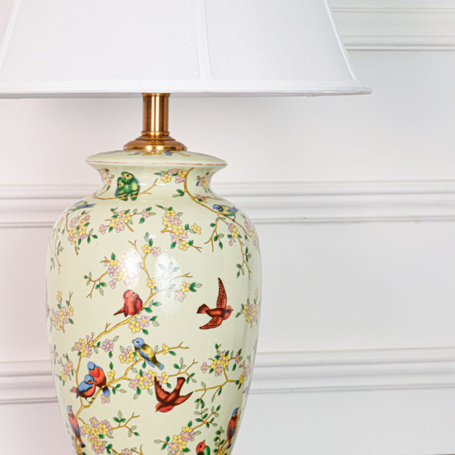 Closeup of green ceramic table lamp showing hand painted birds floral detailing smooth glaze finish and gold metal base.