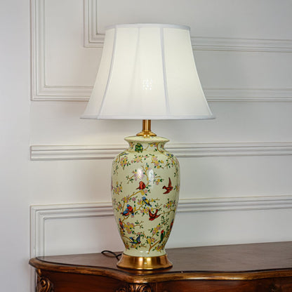 Green ceramic table lamp featuring detailed bird and floral pattern gold metal base and white fabric shade on white background.
