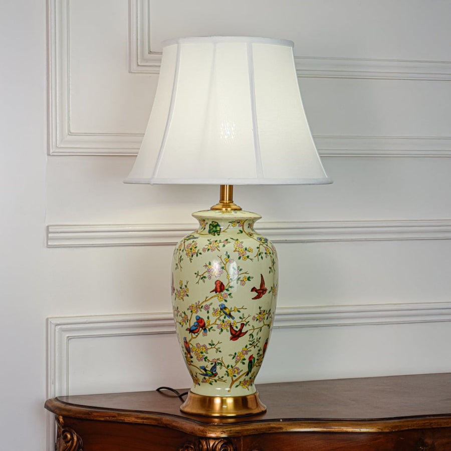 Green ceramic table lamp featuring detailed bird and floral pattern gold metal base and white fabric shade on white background.