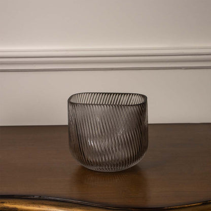 Smoky grey textured glass candle holder with ribbed finish placed on wooden table against neutral wall background for elegant ambient decor appeal.