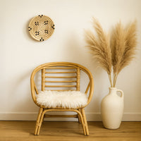 Small beige woven wall basket with black accents hanging on a white wall above a rattan chair with pampas grass for boho home decor.