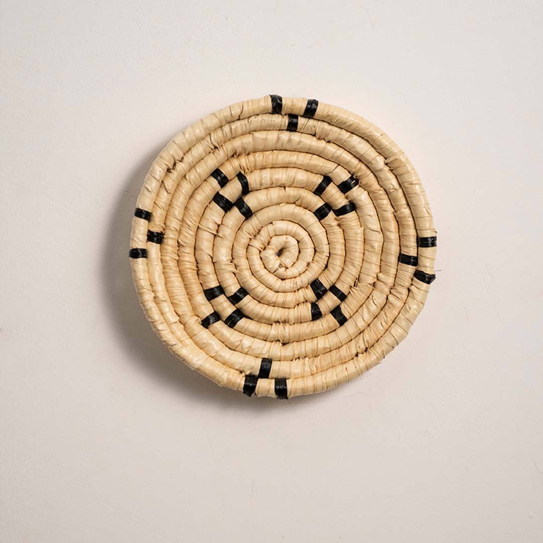 Round woven natural cream seagrass wall basket with small black minimalist stitched accent squares on white background.