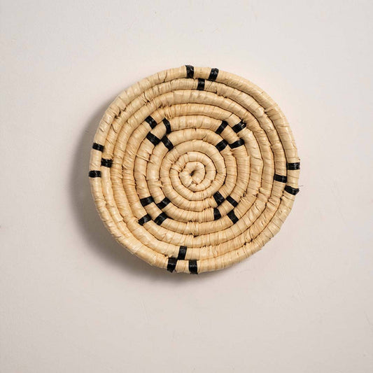 Round woven natural cream seagrass wall basket with small black minimalist stitched accent squares on white background.