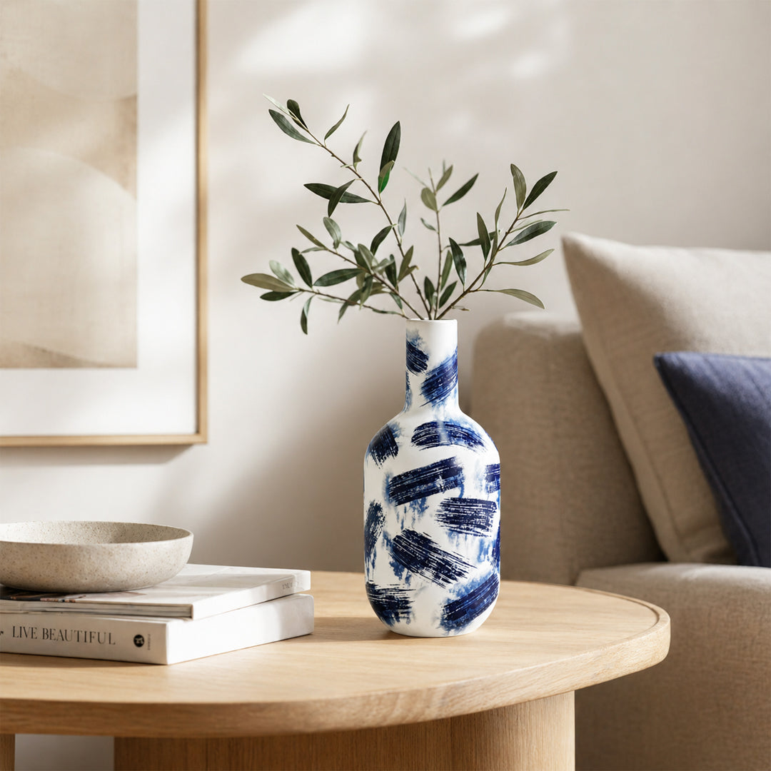 White and blue ceramic flower vase with green stems placed on side table for elegant home decor styling.