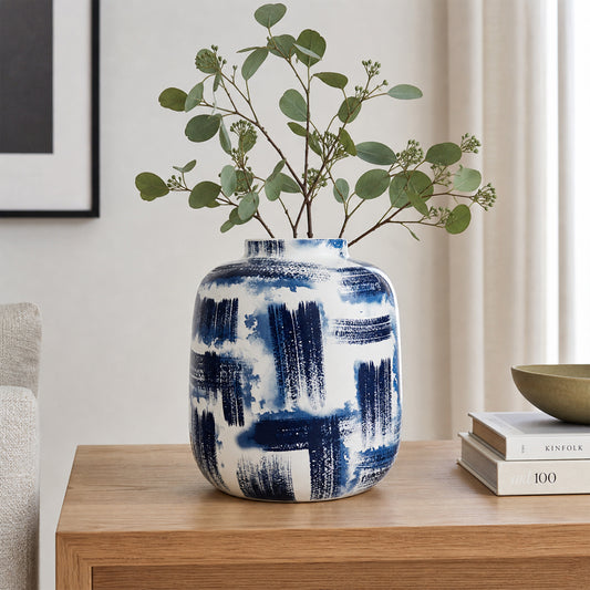 White and blue ceramic flower vase with green stems placed on wooden table for elegant home decor.