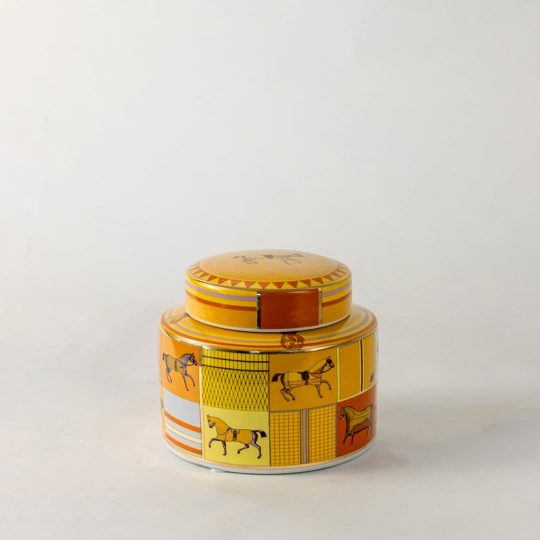 Decorative ceramic jar with lid featuring yellow and orange horse motif pattern on light off white background