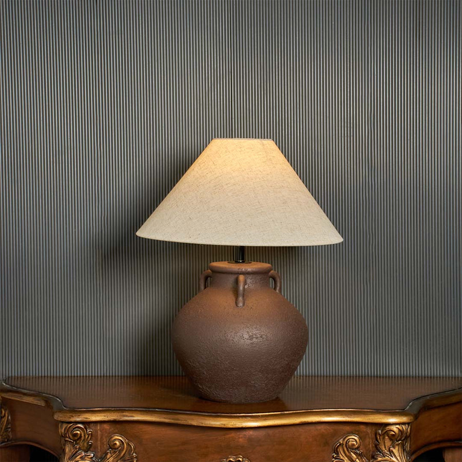 Brown ceramic table lamp with beige linen shade glowing on dark background styled as premium bedside table lamp.