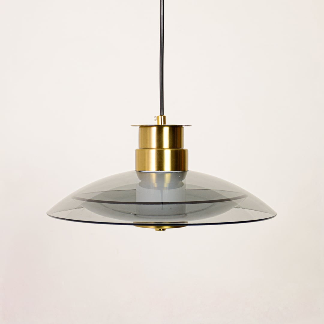Clear glass pendant light with gold metal holder displayed on white background highlighting elegant form and modern lighting style.